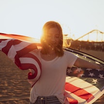 Woman holding an american flag on the beach. Here's how the United States' pluto return in 2022 will...