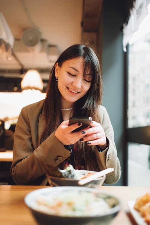 Young beautiful woman using smartphone during lunch in a Japanese restaurant.