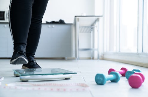 Shot of legs of overweight woman checking her weight scales and drumbell,tape measure beside her.