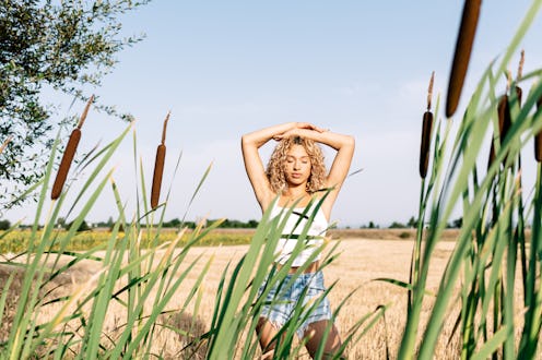 Front view of a blonde curly-haired young woman with eyes closed and her arms raised close to her he...