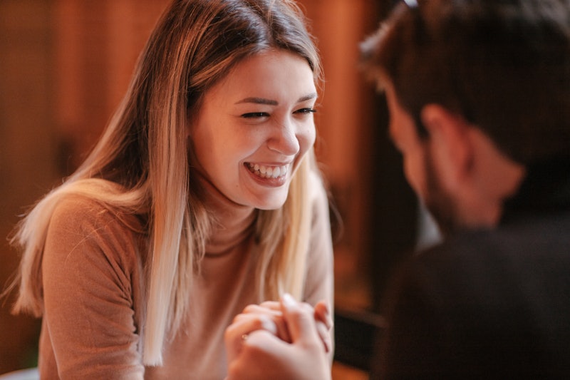 A young woman laughing hard while having a conversation with her partner and holding hands