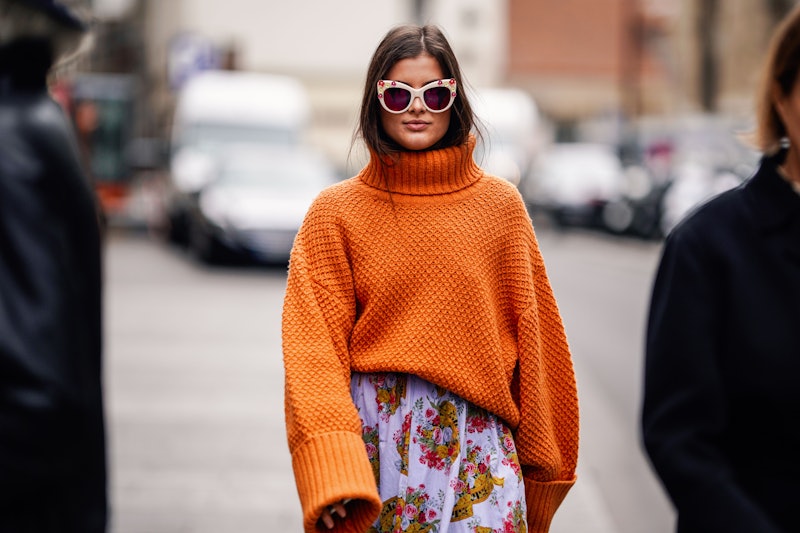 PARIS, FRANCE - MARCH 03: A guest wears an orange oversized pullover, a purple floral print pleated ...