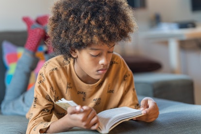 Close-up of a 10 year old African-American boy reading a book lying on the couch at home