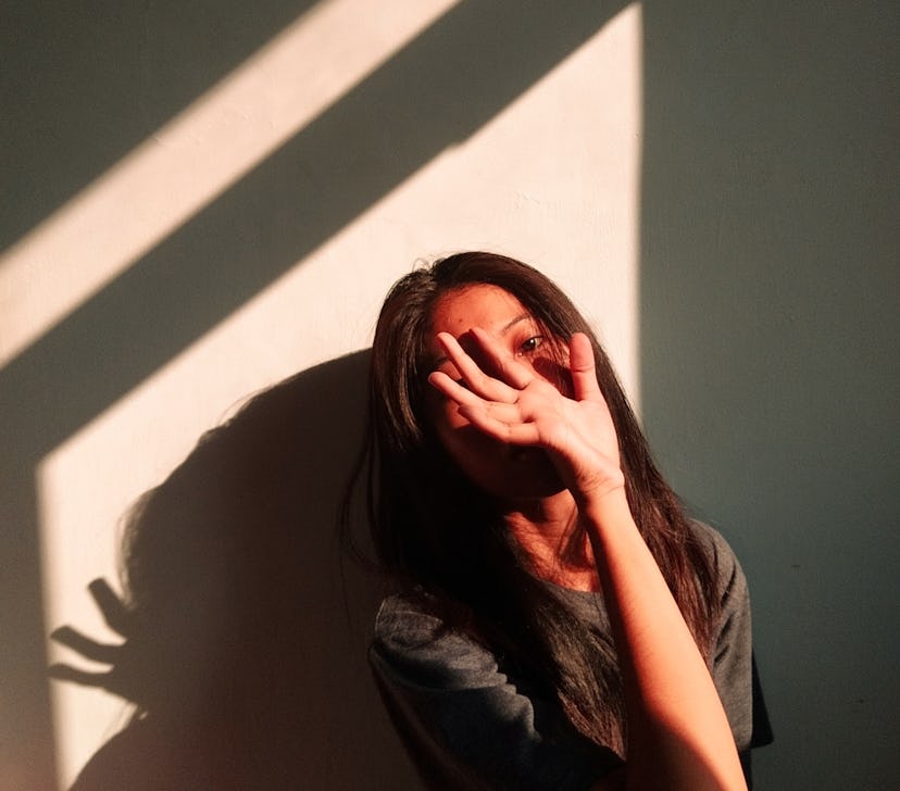 young woman covers her face as she shields light from hitting her face, reflects on zodiac signs mos...