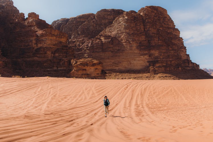 Young female explorer running the sands contemplating the scenic views of the mountains and red dese...
