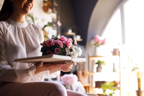 Shot of smiling young woman holding an open book with a beautiful bouquet of flowers on top. Here's ...