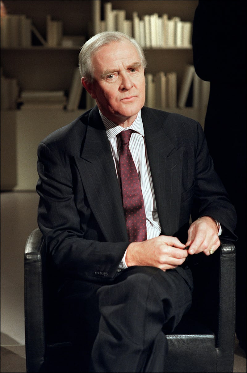 John le Carre in a black suit, striped shirt and maroon tie