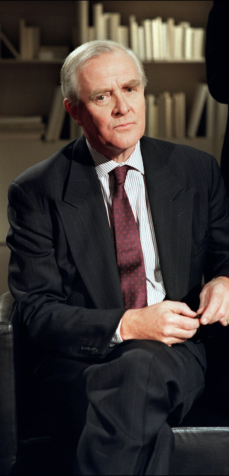 John le Carre in a black suit, striped shirt and maroon tie