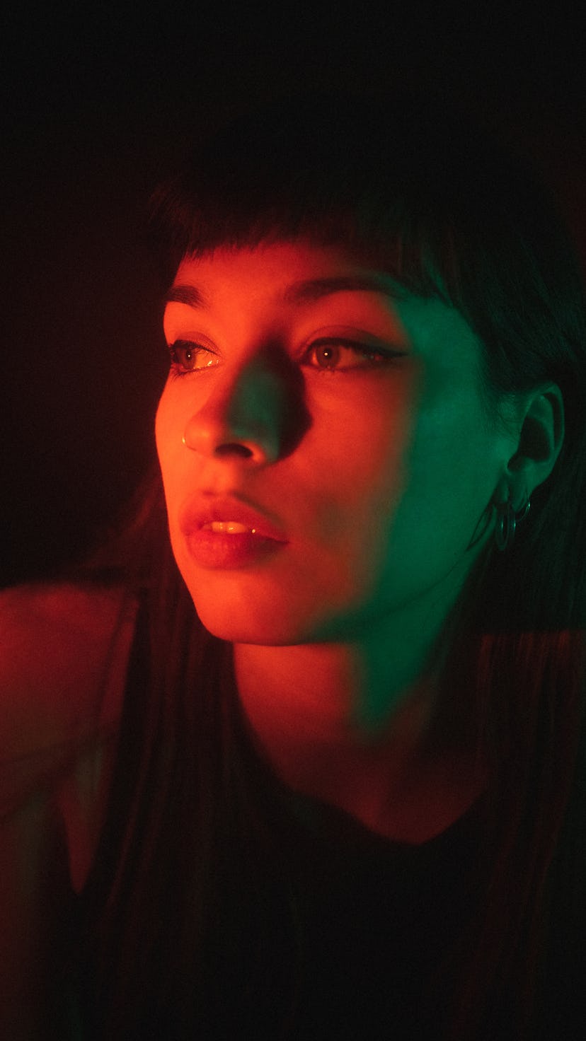 young woman poses while being lit by neon lights as she reflects on the zodiac signs most likely to ...