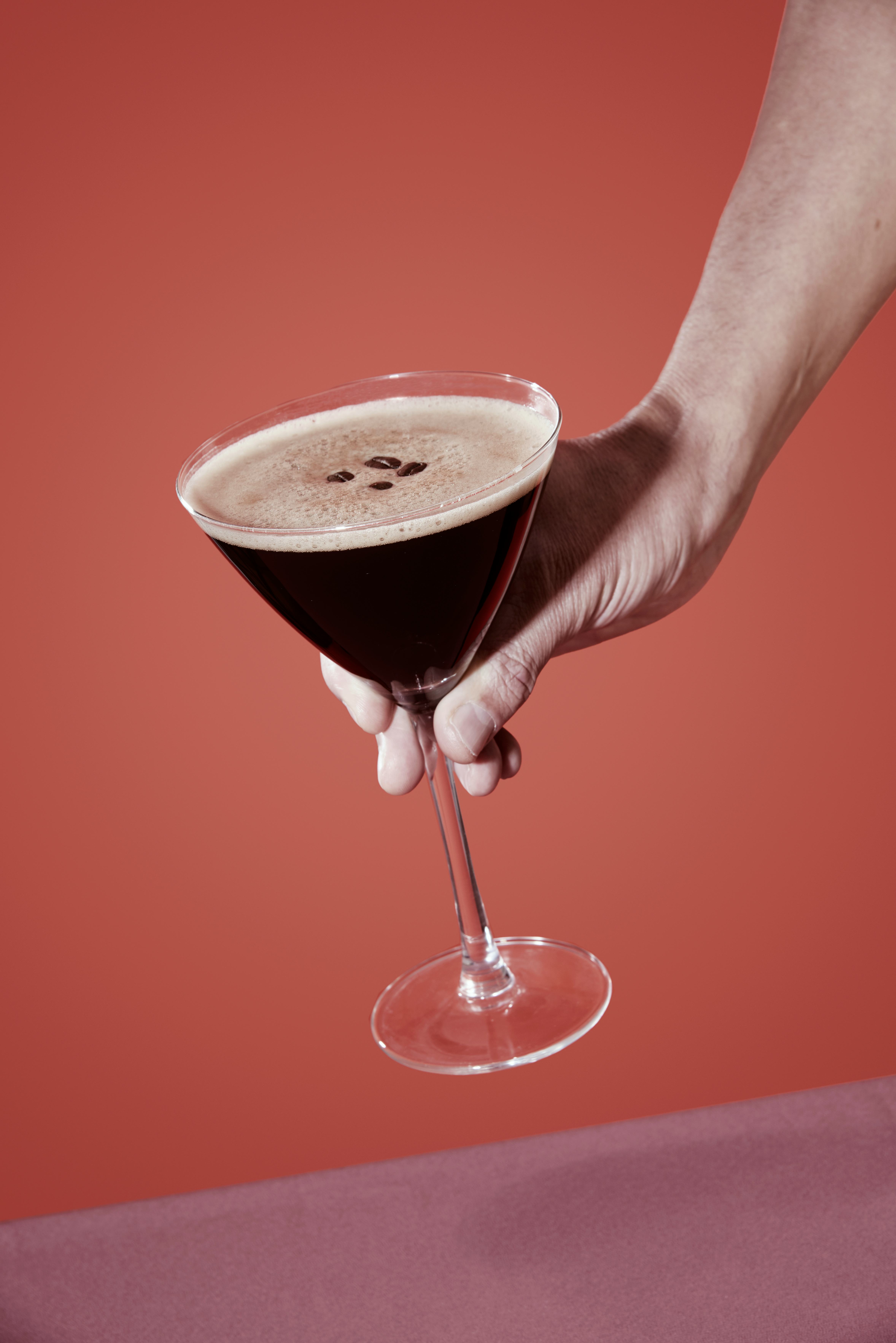 closeup of a man taking or about to leave a glass of espresso martini on a table set with a maroon t...