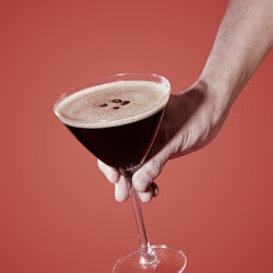 closeup of a man taking or about to leave a glass of espresso martini on a table set with a maroon t...