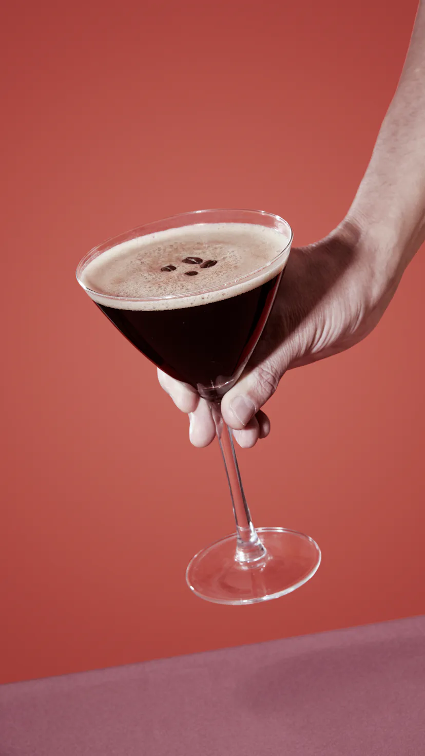 closeup of a man taking or about to leave a glass of espresso martini on a table set with a maroon t...