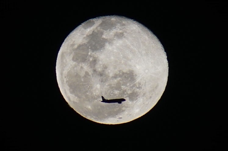 SAN SALVADOR, EL SALVADOR - JANUARY 18: An airplane flights by the moon as it rises in San Salvador,...