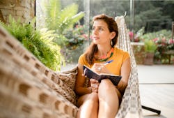 A woman journals while sitting in a hammock. Here's your horoscope for January 24 2022.