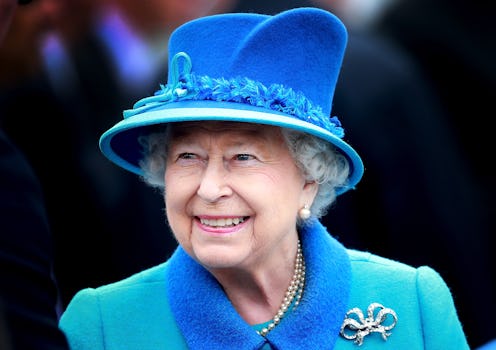 Queen Elizabeth II smiles as she arrives at Tweedbank Station wearing a blue coat and hat.