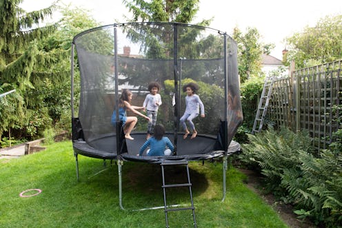 Kids playing about on a trampoline in a back garden during the summer