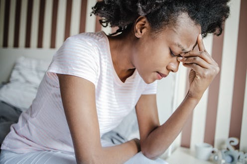 A close-up shot of a woman in bed in her pajamas in the morning. She has a headache and feeling sad