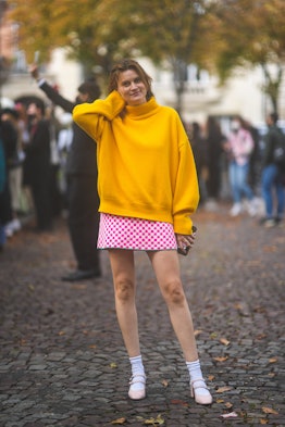 A fashion week attendee is pictured wearing an oversized yellow turtleneck and a neon pink, checkere...