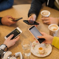 High angle view hands of friends using smart phones and drinking cappuccinos at cafe table