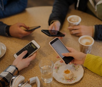 High angle view hands of friends using smart phones and drinking cappuccinos at cafe table
