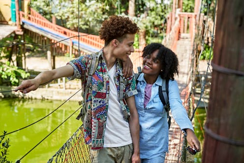 Front view of African-American man and Black woman wearing casual clothing and backpacks, standing o...