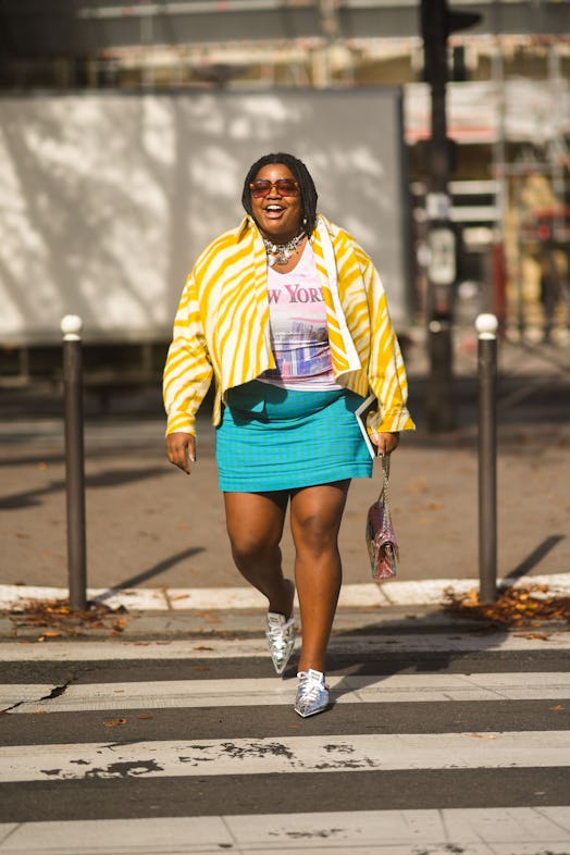 A fashion week attendee pairs a striped jacket, graphic T-shirt and teal mini skirt. 