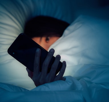Woman hiding under the blanket, chatting and surfing the internet with smart phone at late night on ...