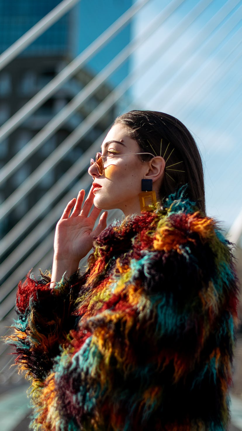 Side view of young stylish female model in colorful fur outfit and sunglasses. The Aquarius 2022 new...