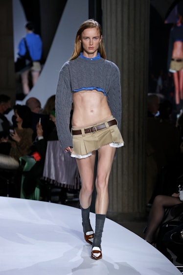 A model wears a tiny khaki belted miniskirt from the Spring 2022 Miu Miu collection.