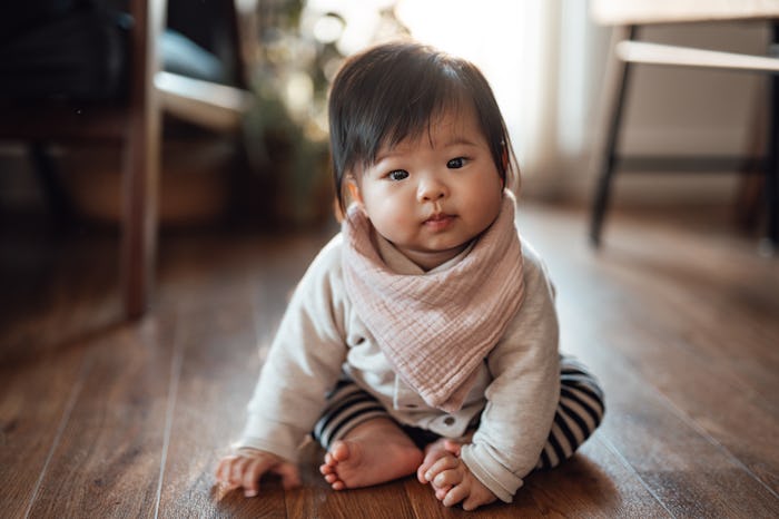 Asian baby girl wearing baby bib sitting on the floor in the living room.