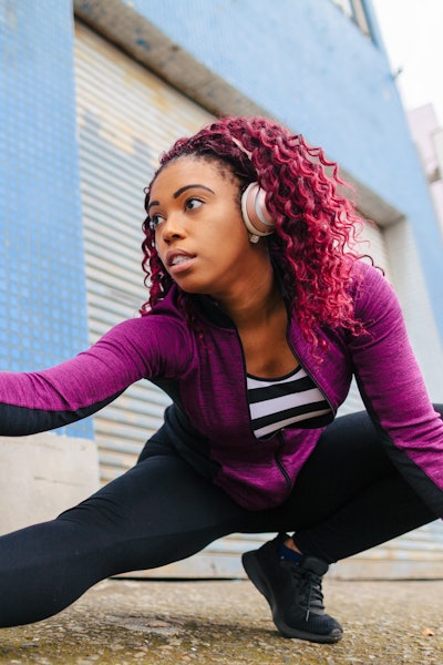 A black woman is warming up in sports clothing in front of a wall in city.