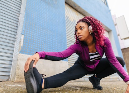 A black woman is warming up in sports clothing in front of a wall in city.