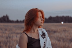 A woman with red hair stands in a field at dusk. Here's your february 2022 new moon horoscope and ho...