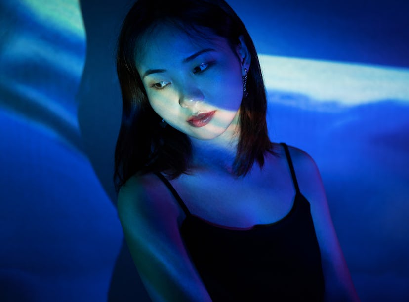 Young woman illuminated by blue projector lighting, thinking about how the February 2022 new moon in...