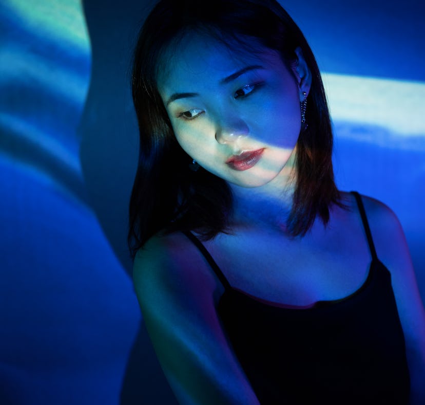 Young woman illuminated by blue projector lighting, thinking about how the February 2022 new moon in...