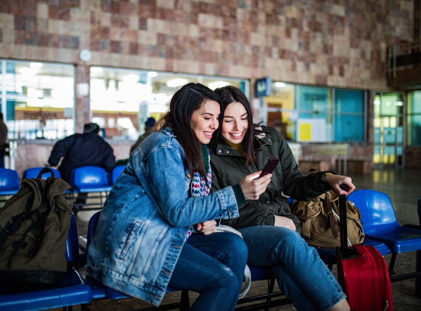 Couple of female friends looking at the smartphone while waiting for the train. Two young women chec...