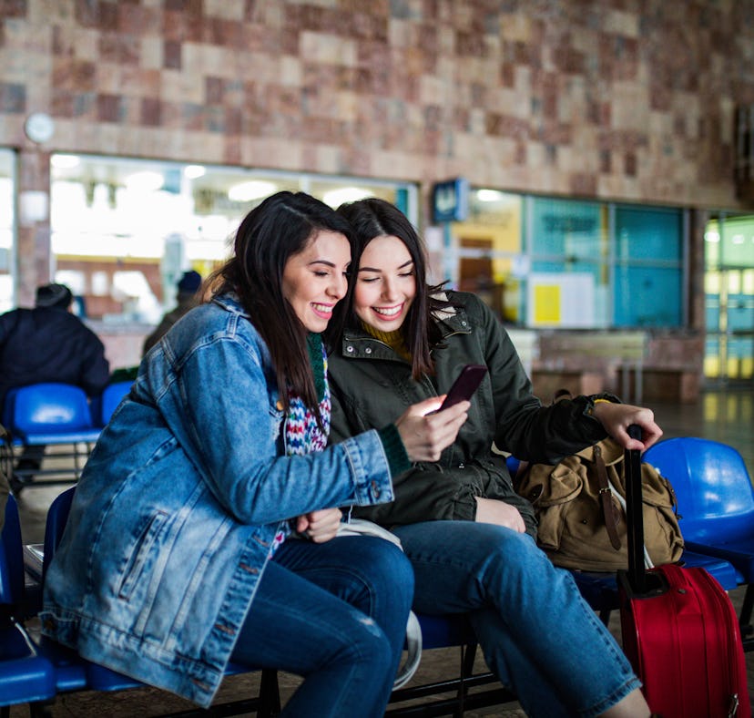 Couple of female friends looking at the smartphone while waiting for the train. Two young women chec...