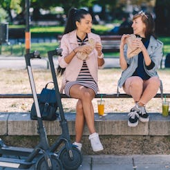 Two friends spending the day in the city park riding motor scooters