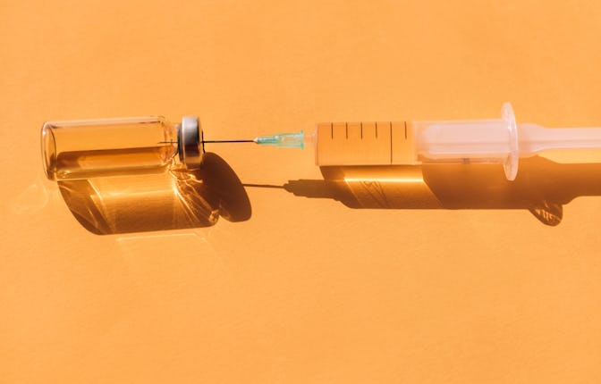 Top view of sterile syringe and opened vial of liquid remedy placed on orange background. Modern syr...