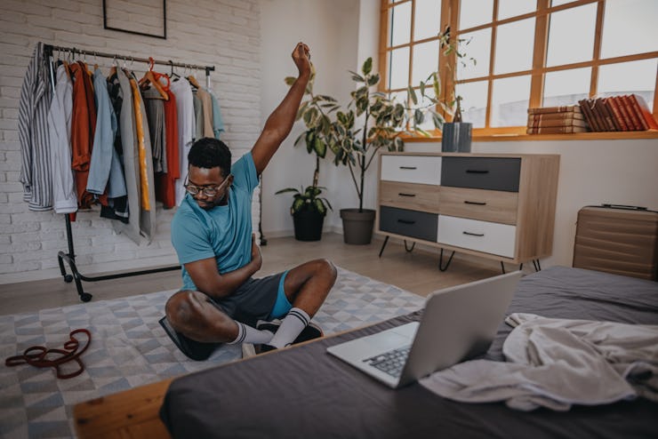 Young athletic man practicing stretching exercise while sitting on floor while watching videos at ho...