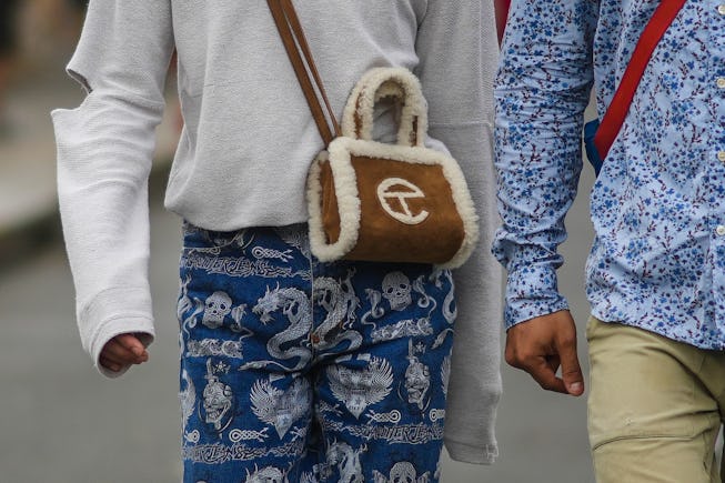 PARIS, FRANCE - JULY 10: A passerby wears a white pullover, a brown suede bag from Telfar with white...