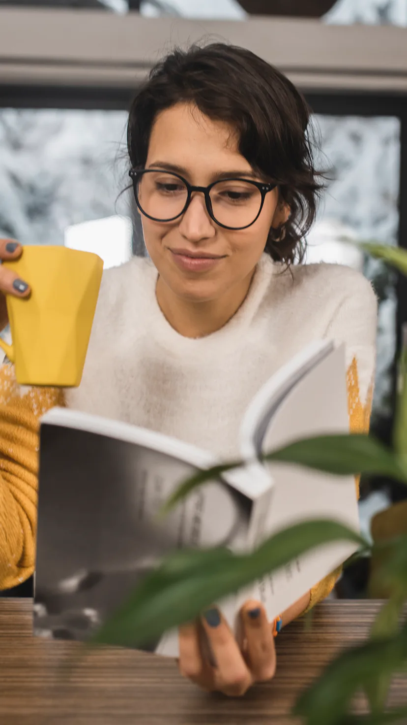 Portrait of a young woman reading a book and enjoying coffee at home.
