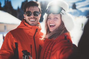 Smiling couple taking photos on ski holiday and using ski captions for their posts on Instagram.
