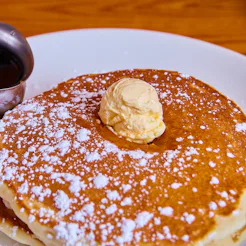 Image of Classic stack of pancakes sprinkled with powdered sugar and topped with butter dollop and s...