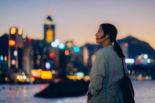 Confident and determined young Asian businesswoman standing by the promenade, looking up to sky, sta...