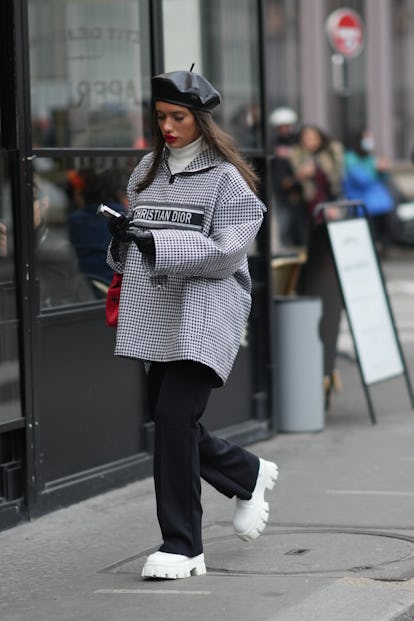 PARIS, FRANCE - JANUARY 27: A guest wears a black shiny leather beret from Dior, a white turtleneck ...