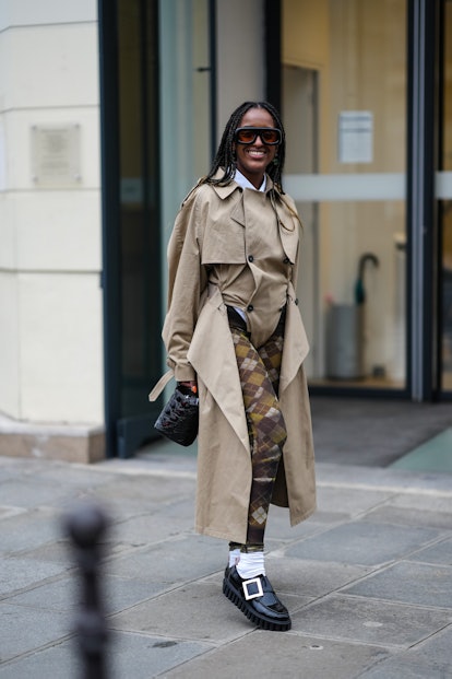 PARIS, FRANCE - JANUARY 26: A guest wears black sunglasses, a white shirt, a beige long trench coat,...