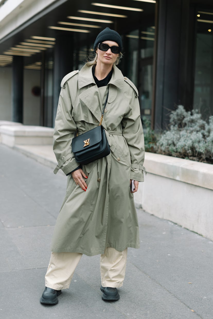 PARIS, FRANCE - JANUARY 27: A guest poses wearing a trench coat, Louis Vuitton bag, black beanie and...