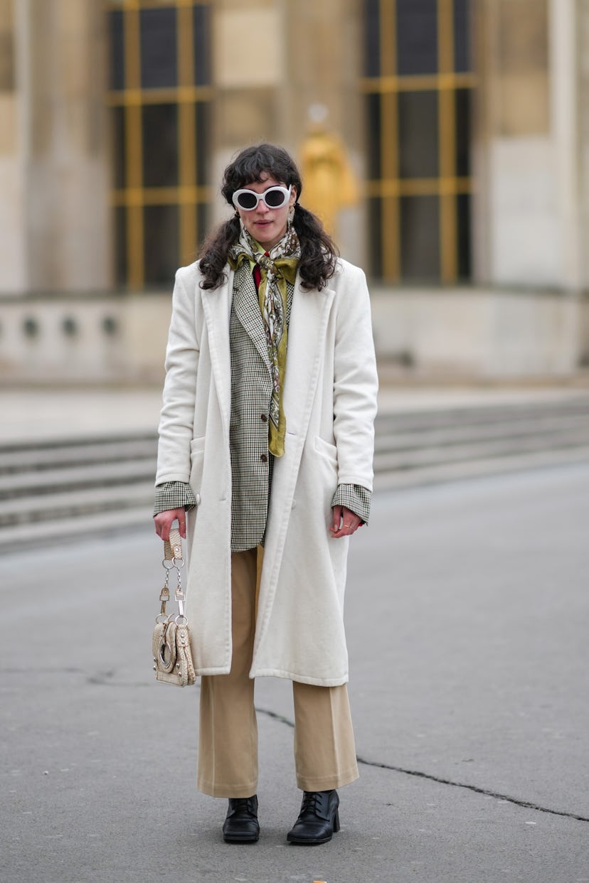 PARIS, FRANCE - JANUARY 25: A guest wears white sunglasses, gold earrings, a khaki / brown / white p...