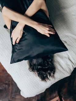 Portrait of young beautiful woman hugging a pillow while lying on her bed at home.
